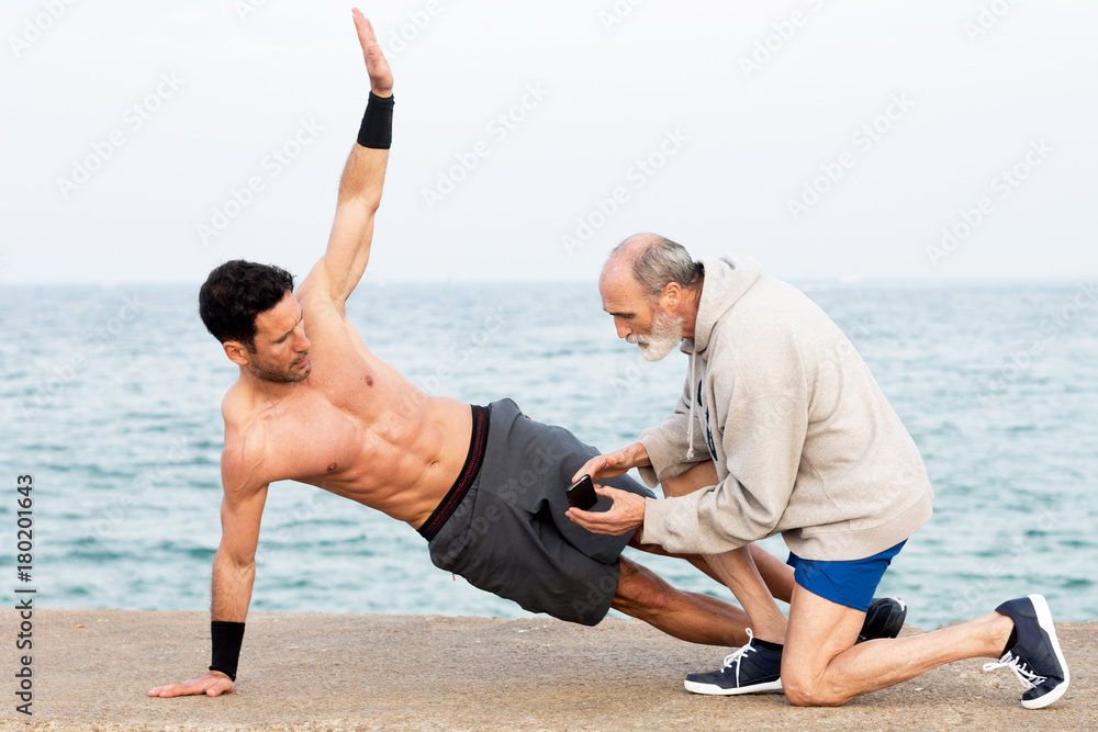 Athletic Man making side plank exercise outside on the waterfront with coach Athletic Man making side plank exercise outside on the waterfront with coach