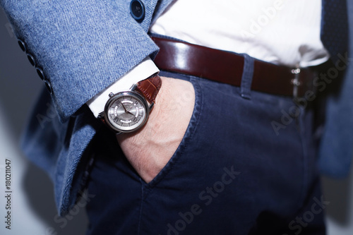 Closeup fashion image of luxury watch on wrist of man.body detail of a business man.Man's hand in wool blue jacket,in dark blue pants pocket closeup.Casual outfit. Tonal in a business suit close up