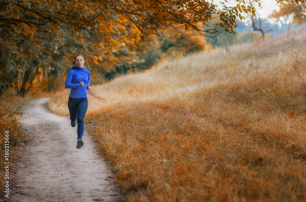 young slim athleic jogger woman runs along the path  on the  beautiful  autumnal forest.