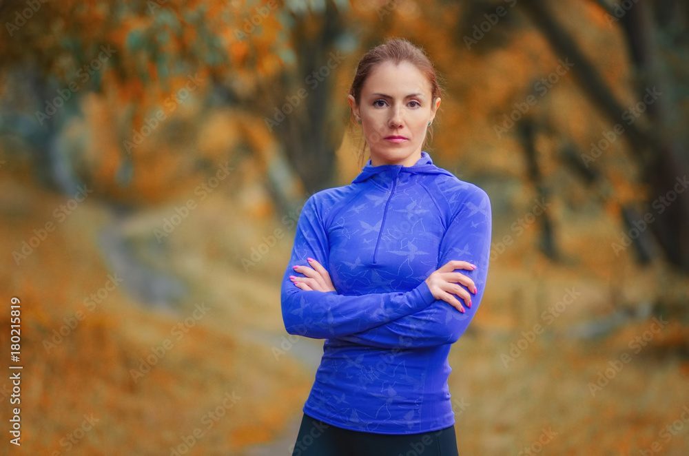 A portrait of the slim athletic woman trainer with crossed arms in a blue jacket in the autumnal forest. A portrait of the slim athletic woman trainer with crossed arms in a blue jacket in the autumnal forest.