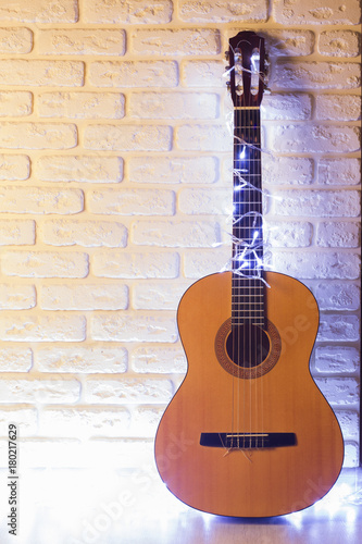 Guitar with lighted garlands on white brick background © GeraKTV