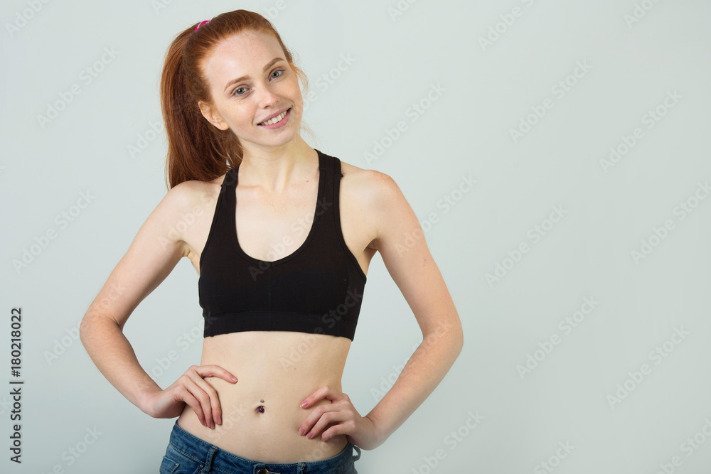 beautiful slender girl with a smile with red hair in sportswear on a light background beautiful slender girl with a smile with red hair in sportswear on a light background