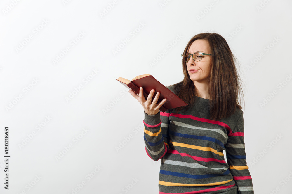 Beautiful European young brown-haired woman in glasses for sight dressed in casual dark grey longsleeve with colorful stripes, standing with book on a white background. Reading and studying concept. Beautiful European young brown-haired woman in glasses for sight dressed in casual dark grey longsleeve with colorful stripes, standing with book on a white background. Reading and studying concept.
