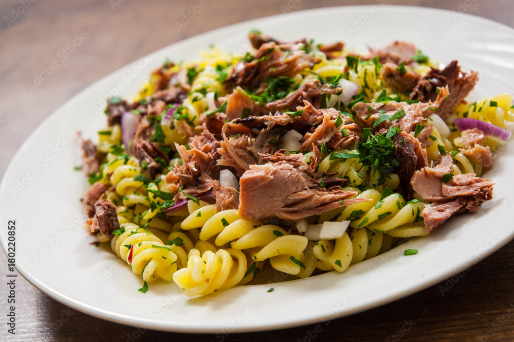 pasta fusilli salad with tuna and onion in white plate on a wooden background pasta fusilli salad with tuna and onion in white plate on a wooden background