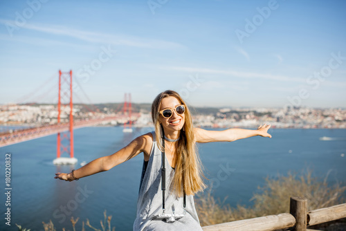 Woman having fun flying with hands on the beautiful landscape view background with iron bridge and river in Lisbon city, Portugal