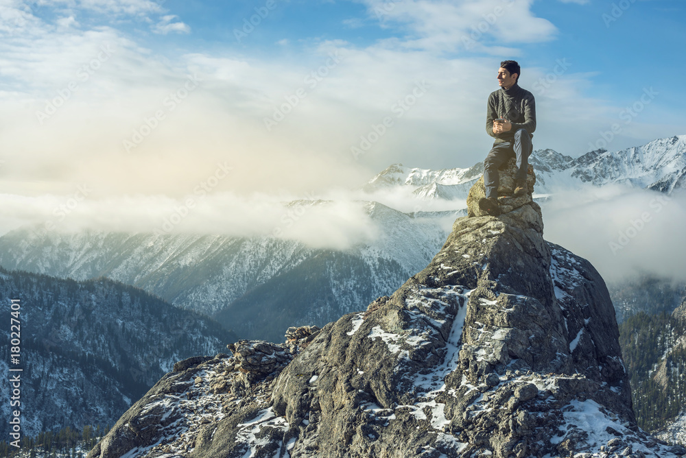 Young man in a sweater with phone in hand on the top of a snowy mountain. Concept availability of mobile connection