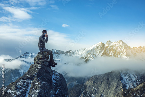 Young man in a sweater with phone in hand on the top of a snowy mountain. Concept availability of mobile connection photo