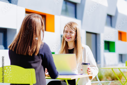 Two female sudents sitting in front to each other in cafe outdoor university campus. photo