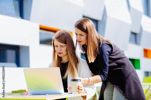 Two female co-workers browsing laptop outdoor together - searching social networking technology concept. photo