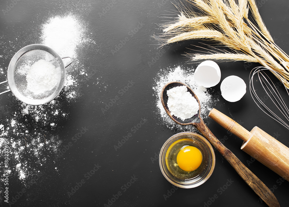 Baking ingredients. Bowl, eggs, flour, eggbeater, rolling pin and eggshells on black chalkboard 