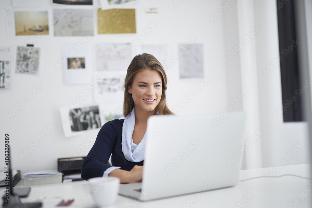 Smiling young woman using laptop at desk in office Smiling young woman using laptop at desk in office
