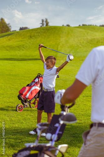 Boy practice golf with his father or trainer at golf course on warm autumn day