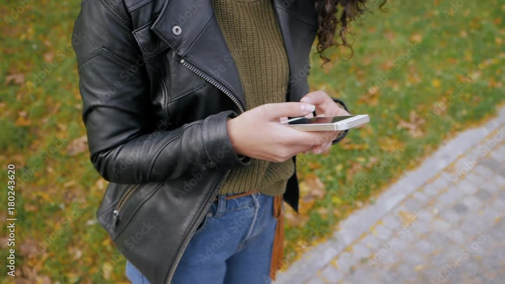 unrecognizable woman's hand texting, sending sms on smartphone in the autumn park. Curly haired latin or afro-american girl with mobile phone, slow motion, dolly shot. unrecognizable woman's hand texting, sending sms on smartphone in the autumn park. Curly haired latin or afro-american girl with mobile phone, slow motion, dolly shot.