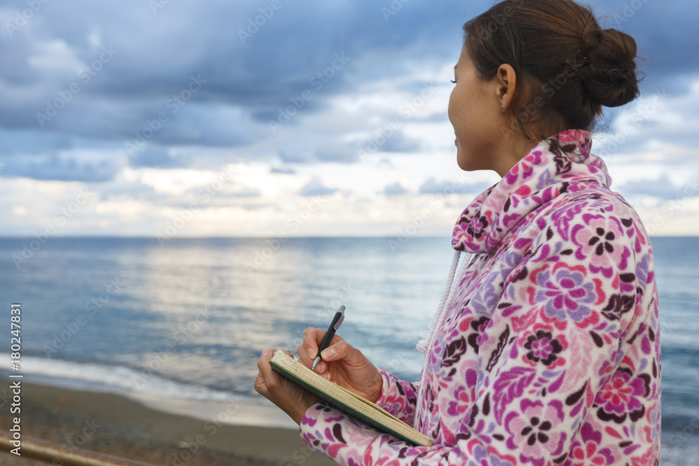 Fototapeta premium A girl is writing on a beach. Copywriter. Author. Literature. Creativity. Freelancer