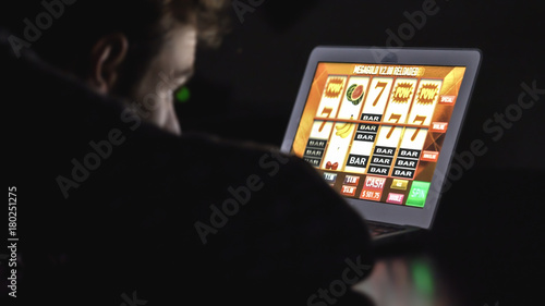 Gambling addicted man in front of online casino slot machine on laptop computer at night - loosing his money. Dramatic low light grain shot. photo