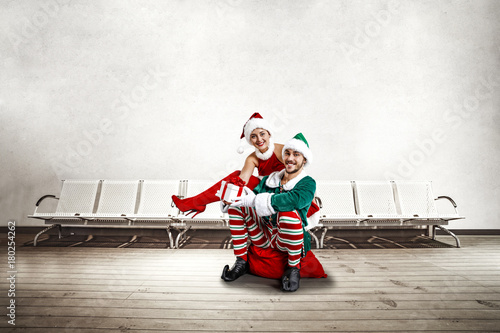 Two Christmas elves in the waiting room. a large wooden floor, white chairs and a white wall with space for your inscription. Christmas advertising background.