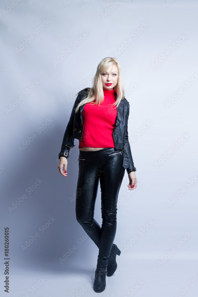 Full-length portrait of a young blond woman. The girl is dressed in black leather trousers and a jacket. Model poses against white background in studio. Full-length portrait of a young blond woman. The girl is dressed in black leather trousers and a jacket. Model poses against white background in studio.