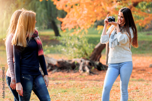 Young woman photographing her friends in park  © lordn