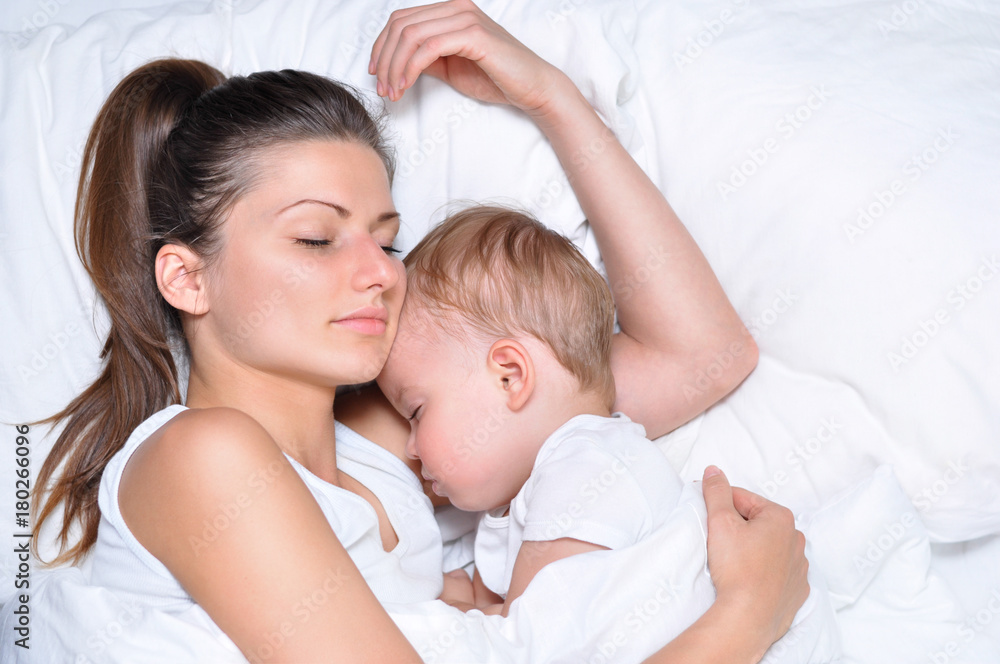 young beautiful mother hugs with her sleeping little cute son on white linen young beautiful mother hugs with her sleeping little cute son on white linen