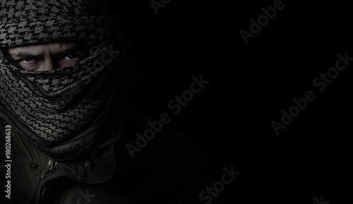 angry soldier in a camouflage scarf shemag on a black background photo