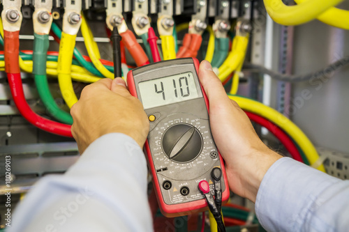 Multimeter in hands of electrician in power high voltage three phase circuit box close-up. Engineer hands with tester measured. Electric fuse panel.