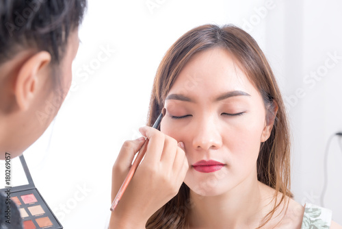 Makeup artist is makeup a asian woman model on white background Before take a photo in studio