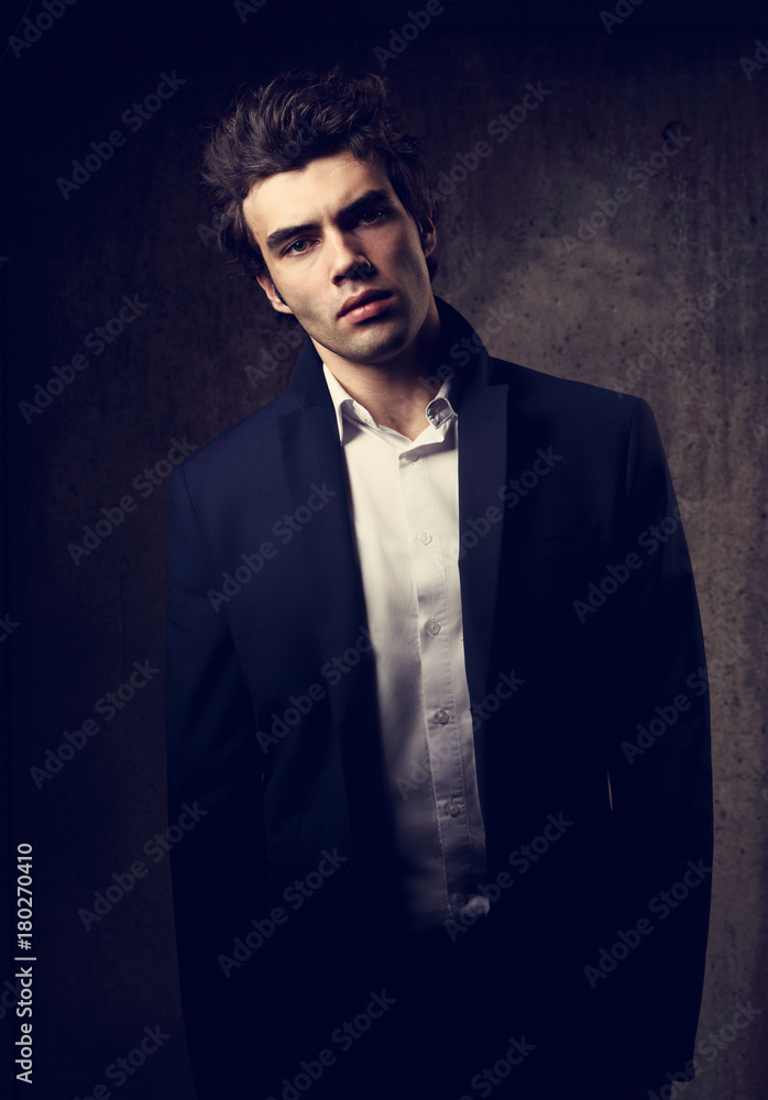 Fototapeta premium Handsome male model posing in fashion suit and white style shirt looking on dark shadow background. Closeup portrait