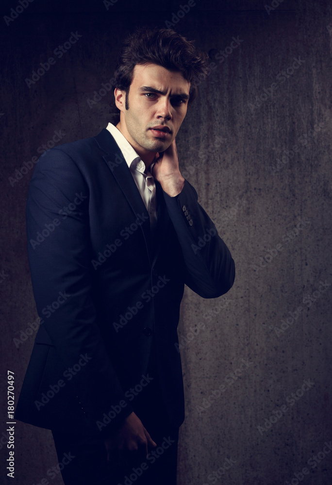Charismatic handsome male model posing in blue fashion suit and white style shirt looking on dark shadow background. Charismatic handsome male model posing in blue fashion suit and white style shirt looking on dark shadow background.