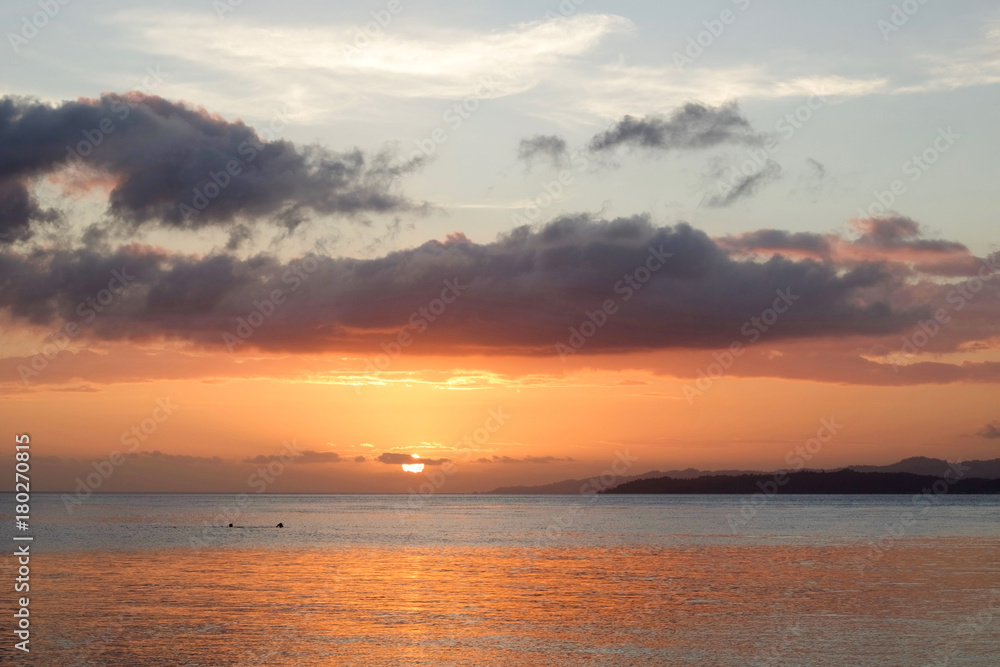 beautiful sunset over a tropical sea with two people doing snorkeling