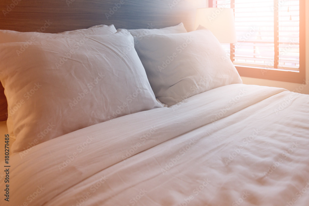 Bed maid-up with clean white pillows and bed sheets in beauty room. Close-up. Lens flair in sunlight. Bed maid-up with clean white pillows and bed sheets in beauty room. Close-up. Lens flair in sunlight.