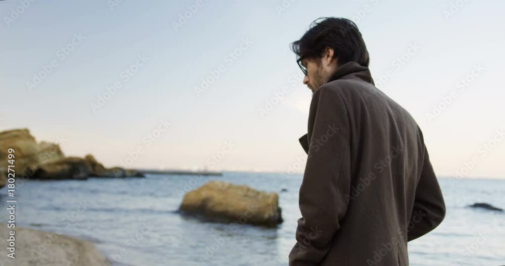 View from back on handsome depressed man strolling at the rocky seacoast and thinking in the morning. Outdoors View from back on handsome depressed man strolling at the rocky seacoast and thinking in the morning. Outdoors