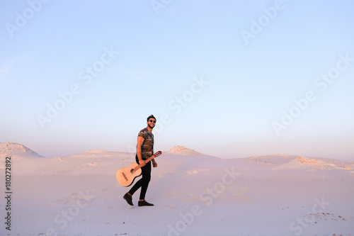 Stately Muslim young man walks with guitar in hands through dese photo