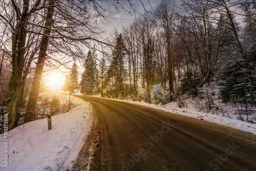 asphalt road through winter forest at sunset. beautiful transportation scenery