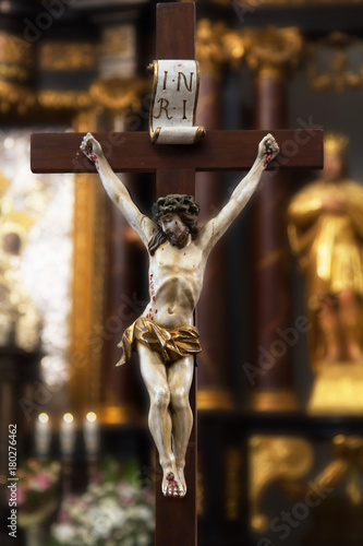 Figure of Jesus Christ hanging on a wooden cross with a faded altar, wreaths and Fototapet