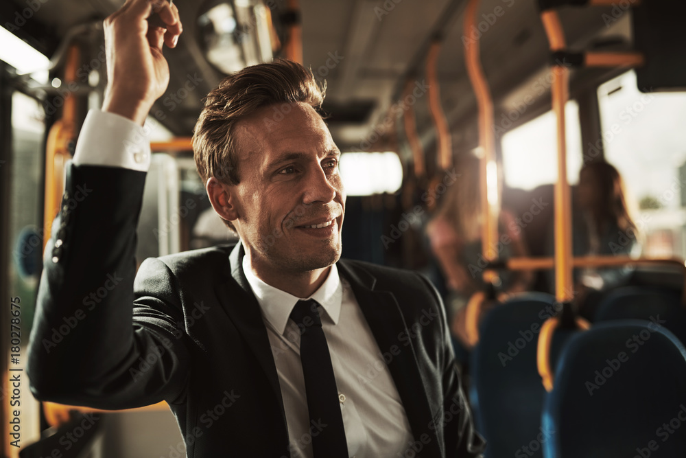 Smiling businessman standing on a bus during his morning commute - obrazy, fototapety, plakaty 