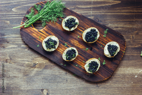 Top view of black caviar appetizers at wooden board.