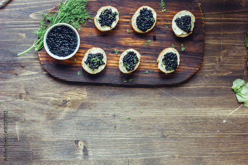 Top view of black caviar appetizers at wooden board.