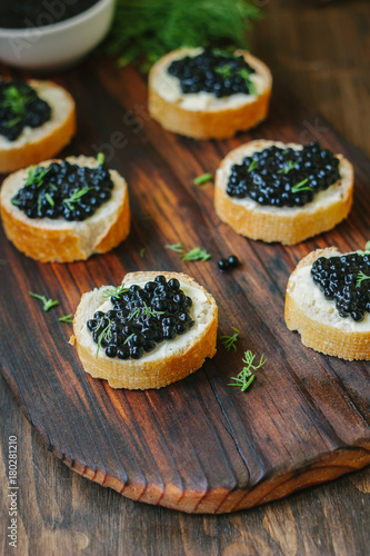 Black caviar on the pieces of bread over wooden kitchen board.