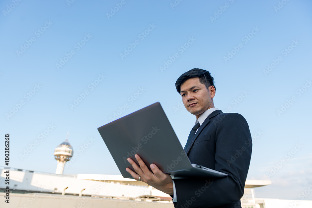 Businessman working with laptop on the roof of building in the evening, Businessman working with laptop on the roof of building in the evening,