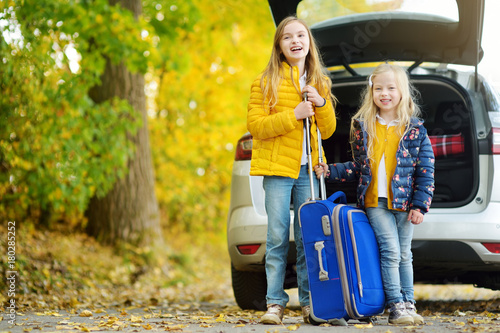 Two adorable girls with a suitcase going on vacations with their parents. Two kids looking forward for a road trip or travel. Autumn break at school. photo