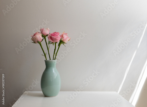 Pink roses in green vase on white table against neutral background with window light