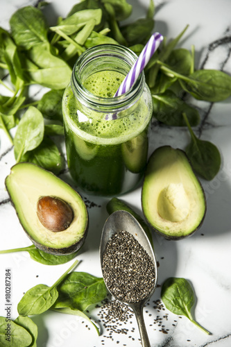 Healthy green smoothie with spinach in a bottle with spinach leaves and fresh avocado on a marble table