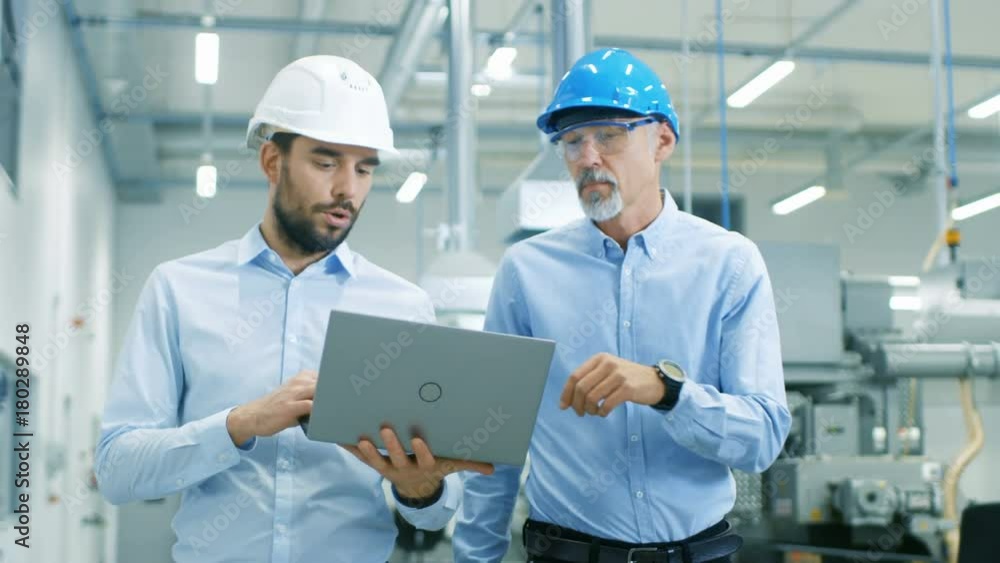 Head of the Project Holds Laptop and Discusses Product Details with Chief Engineer while They Walk Through Modern Factory. Head of the Project Holds Laptop and Discusses Product Details with Chief Engineer while They Walk Through Modern Factory.