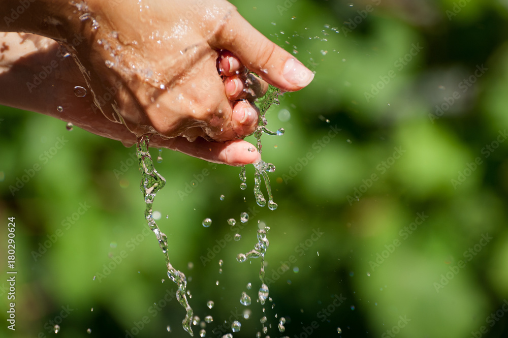 Fototapeta premium Woman washing hand outdoors. Natural drinking water in the palm. Young hands with water splash, selective focus
