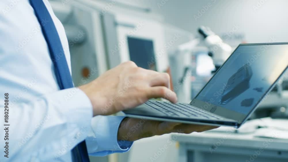 Close-up of the Engineer Holding Laptop with CAD Component Model on Screen. In the Background Modern Factory Equipment. Shot on RED EPIC-W 8K Helium Cinema Camera. Close-up of the Engineer Holding Laptop with CAD Component Model on Screen. In the Background Modern Factory Equipment. Shot on RED EPIC-W 8K Helium Cinema Camera.