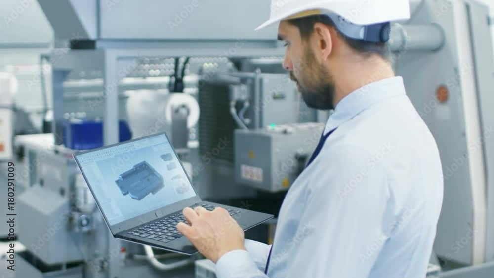 Chief Engineer in the Hard Hat Holds Laptop with 3D Component Model on it's Screen. In the Background Modern Factory Equipment. Shot on RED EPIC-W 8K Helium Cinema Camera. Chief Engineer in the Hard Hat Holds Laptop with 3D Component Model on it's Screen. In the Background Modern Factory Equipment. Shot on RED EPIC-W 8K Helium Cinema Camera.