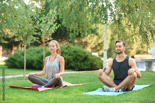 Young man and woman meditating on yoga mats in park