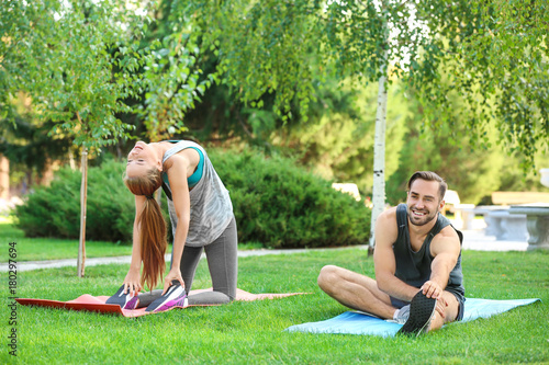 Young man and woman doing exercises on yoga mats in park