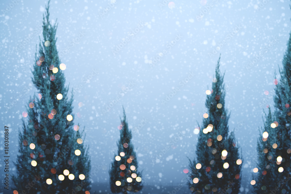 Blurred of Christmas tree and light bokeh with snowfall on sky background in winter. vintage color tone and rustic style.