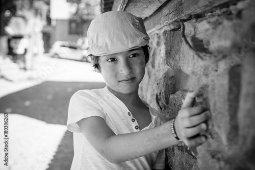 Portrait of a boy in a T-shirt and a cap near the stone wall. Black and white.
